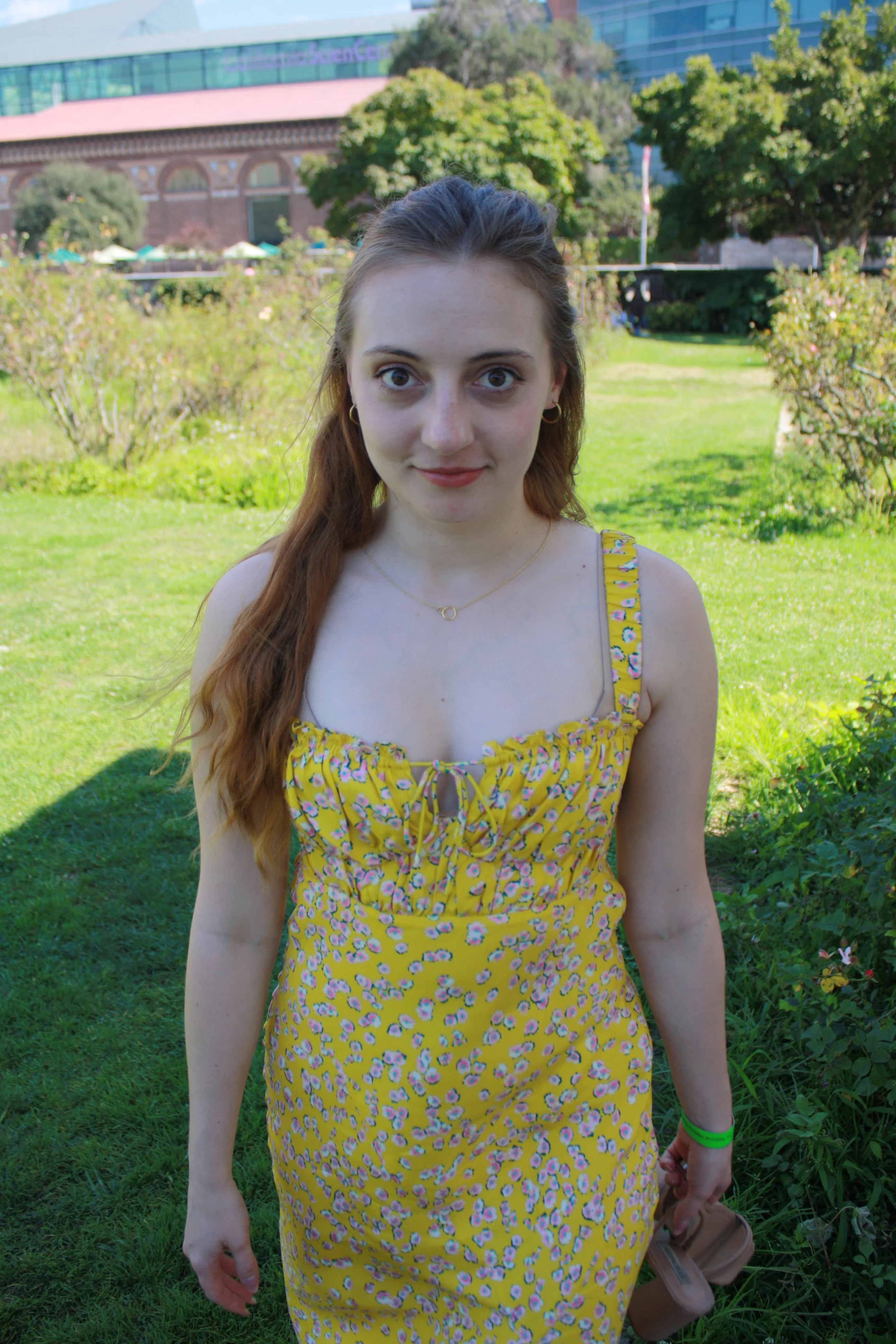 Jordie Morris facing the camera in a yellow floral dress on the garden lawn at the Exposition Park Rose Garden.